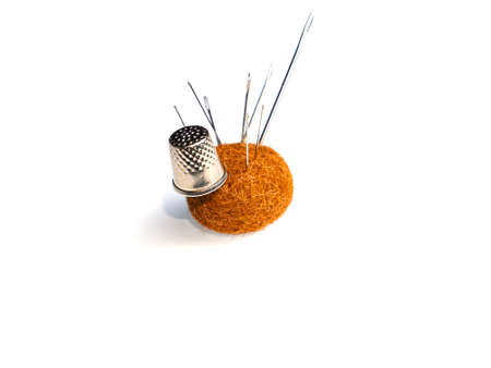 Soft fabric cushion with stuck-in needles and metal sewing thimble. A pillow with photknuts with...
