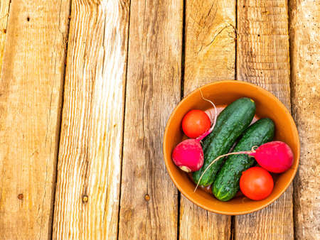 Vegetables cucumbers with tomatoes and radishes in a plate. Green cucumber. Red tomato. Red radish. Vegetable salad. Ceramic tableware. Wooden table. Vegetarian food. Healthy eating.の写真素材