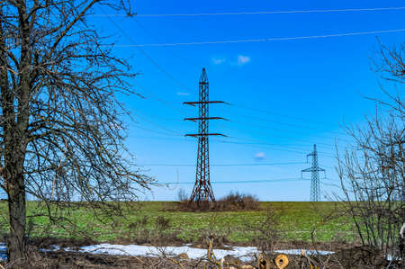 High-voltage power transmission tower with wires. High voltage line. Energy industry. Energy transfer. Blue sky. White clouds. Agricultural field. Cloudy horizon. Business. Electrician work.の写真素材