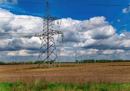 High-voltage power transmission tower with wires. High voltage line. Energy industry. Energy transfer. Blue sky. White clouds. Agricultural field. Cloudy horizon. Business. Electrician work.の写真素材
