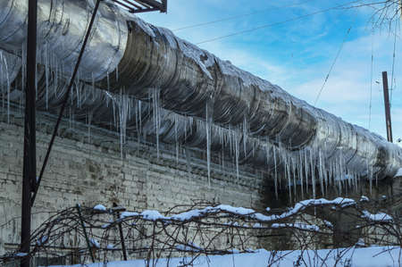 Ice icicles on a metal pipe of an industrial pipeline. Industrial equipment. Gas pipeline. North. Flow. Ventilation system. Winter season. Frozen water. Blue sky.の写真素材