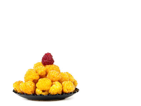 Berries of yellow and red raspberries in a black plate on a white background.