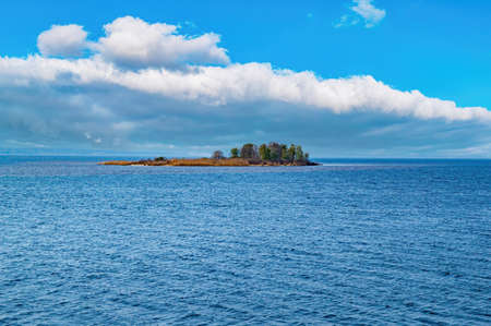 Uninhabited island in the sea against a blue sky with clouds. Island with trees. sea horizon. Blue...