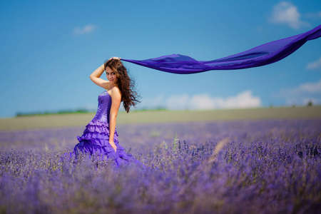 Portrait of beautiful romantic woman in fairy field of lavender with a colored tissue の写真素材