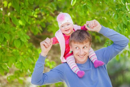 Smiling young father and daughter in a park. Happy dad carrying his baby on his back.の写真素材