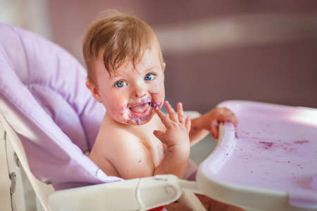 Adorable baby eating on baby chair and making a mess.の写真素材