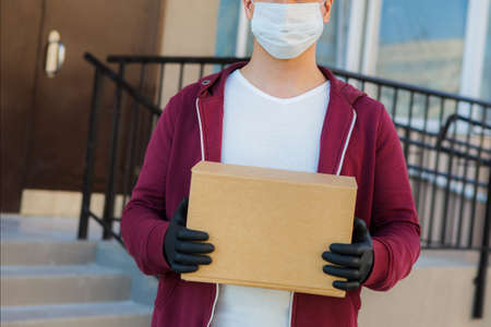 Courier in medical rubber gloves and protective mask holding cardboard boxes. Delivery service. Quarantine.の写真素材