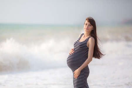 Beautiful pregnant woman in black dress on the beach.の写真素材