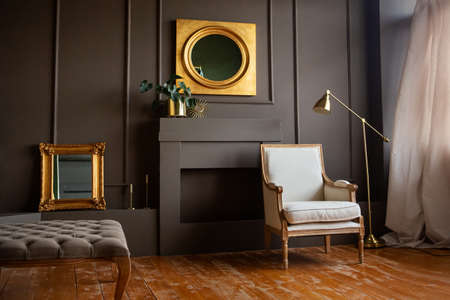 Stylish grey chair against a dark gray wall. Fashionable living room interior, next to a lamp and mirrow.の写真素材