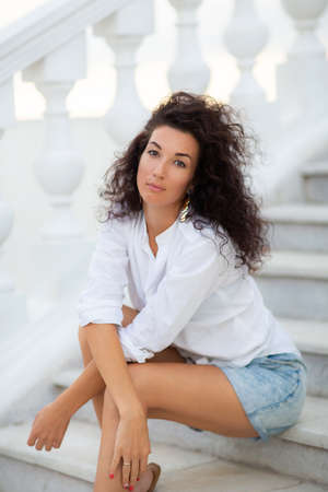 Smiling brunette woman with curly hair on vacation. Happy woman posing outdoors.の写真素材