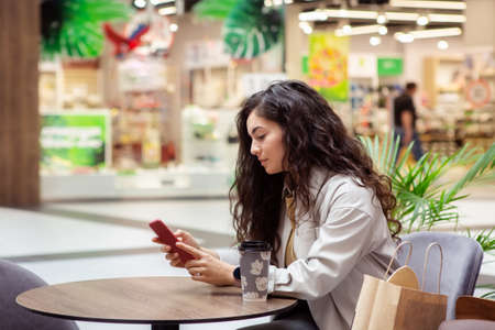 Young woman using smartphone and drinking take away coffee in paper cup.の写真素材