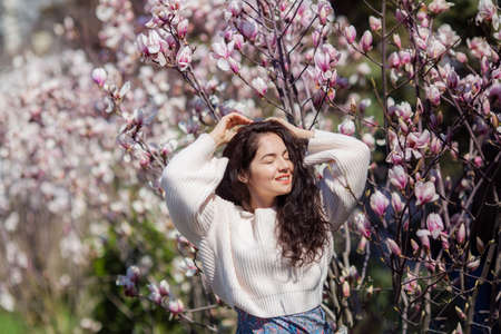 Beautiful girl with flowers of magnolia. Portrait of young smiling brunette woman under blossom magnolia tree.の写真素材