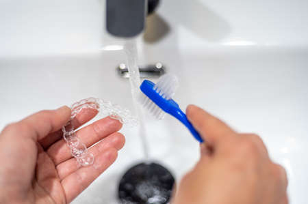Young woman cleaning an invisible dental aligner with a brushの写真素材