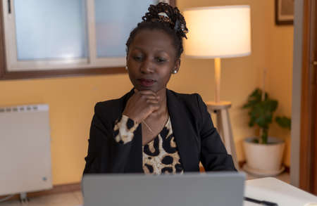 portrait of Young black woman speaking on the phone with animal print top working with a laptopの写真素材