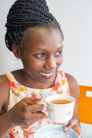 Young woman smiling and drinking tea using a vintage porcelain cup with flowers patternの写真素材