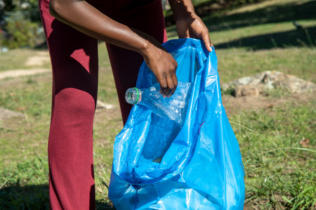 Young woman cleaning up plastics from field. Collecting garbage in a plastic bagの写真素材