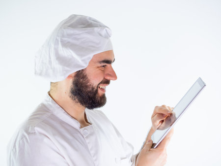 Young male chef using a tablet, reading a recipe. Isolated on a white backgroundの写真素材