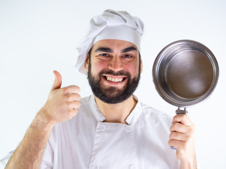 Young male chef showing a stainless saucepan while smiling and looking at camera. Isolated on a white backgroundの写真素材
