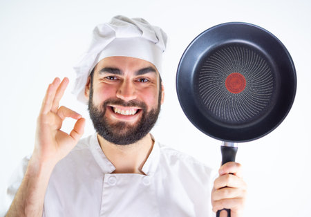 Young male chef showing a non stick pan while smiling and looking at camera. Isolated on a white backgroundの写真素材