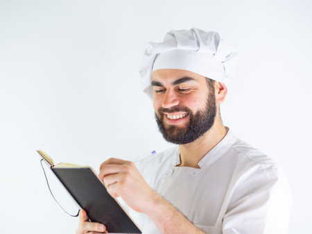 Young male chef using a notebook, writing a recipe. Isolated on a white backgroundの写真素材