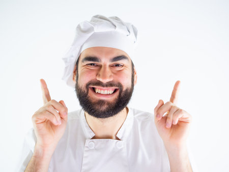 Young male chef pointing up with both hands while smiling and looking at camera. Isolated on a white backgroundの写真素材