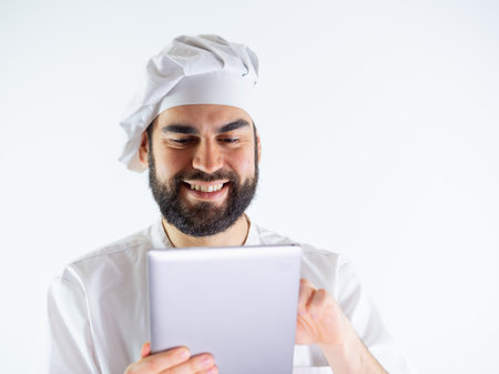 Young male chef using a tablet, reading a recipe. Isolated on a white backgroundの写真素材
