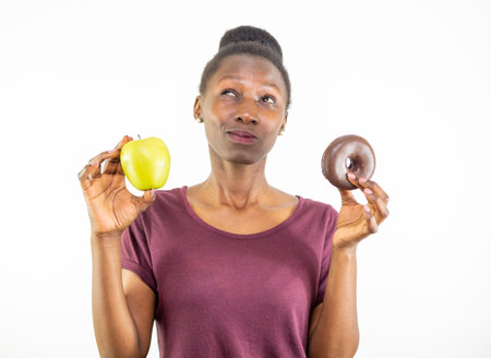 Young woman choosing between healthy food and junk food isolated on white backgroundの写真素材