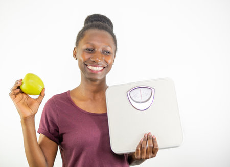 Young woman holding a weight scale and a green apple isolated on white background