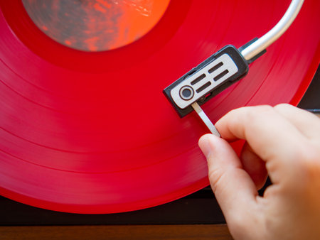 Detail of a male hand placing the needle on the track of a red vinyl record. vintage turntable