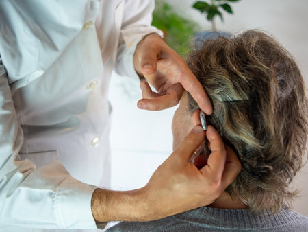 Young audiologist helping to insert an electronic hearing aid to an old woman patientの写真素材