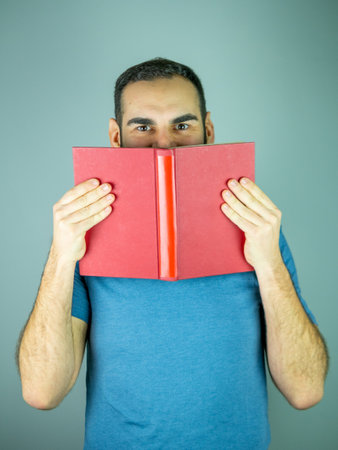 Young man hiding part of his face with red cover book Looking at cameraの写真素材