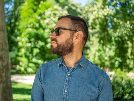 Portrait of a handsome bearded man in a blue shirt and sunglasses in the parkの写真素材