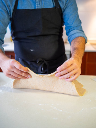 Young man using his hands to stretch a fresh wheat flour dough