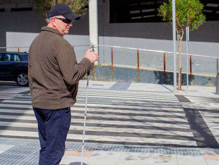 A sightless man patiently waits at the crosswalk for the moment to cross the street safelyの写真素材