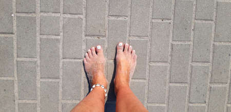 Tanned and sandy feet with white nail varnish and seashell anklet on the concrete background