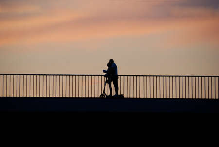 Silhouette of a couple riding a scooter on a bridge at sunsetの写真素材