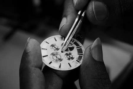 Black and white closeup photograph of a watchmaker examining the dial of a watch under a light source using tweezer.の写真素材