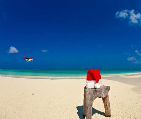 Santa hat is on an original stool  is made from trunk of tree with seaplane, Maldives beachの写真素材