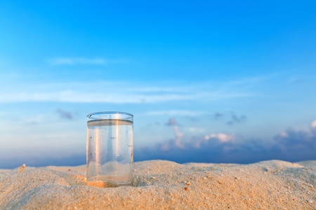 Glass of water is on a coral sandy beachの写真素材