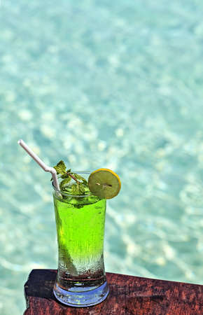 Glass of the green soft drink is on a beach table (Maldives, The Indian Ocean)の写真素材