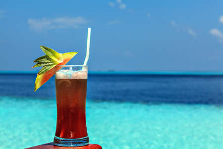 Glass of the soft drink is on a beach table (Maldives, The Indian Ocean)の写真素材
