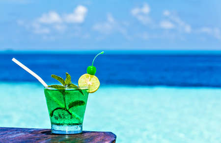 Glass of the soft drink is on a beach table (Maldives, The Indian Ocean)の写真素材