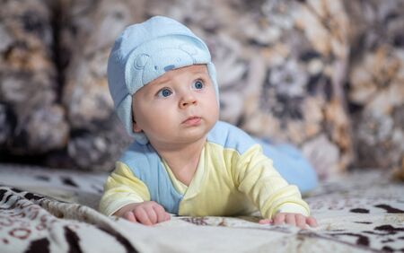 Little toddler boy in pajamas and a hat. A small child, a baby, learns the world, lies on his tummy, looks away.の写真素材