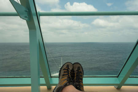 Resting on a sun lounger with feet crossed and looking ahead at the view of the ocean and the horizon while on a cruise ship.の写真素材