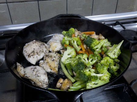 A mix of vegetables and chicken mixed with herbs, pepper and salt being cooked on a cast iron skillet.の写真素材