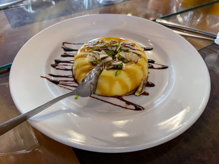 Caramel custard served in a white plate topped with sliced almond and pistachios.