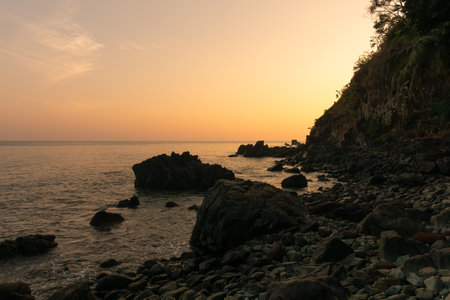 beautiful picturesque glow of sunset behind the hill as seen from a beach with a rocky shoreline.の写真素材
