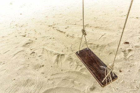 Empty wooden rope swing hang isolated above a white sand beach.