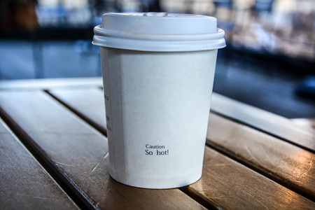 White  hot coffee paper cup with caution word "so hot!" isolated on wooden table with morning sunlightの写真素材
