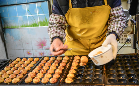 Making Takoyaki, a ball-shaped Japanese snack made of a wheat flour-based batter and cooked in a special molded pan. Japanese street food stall.の写真素材